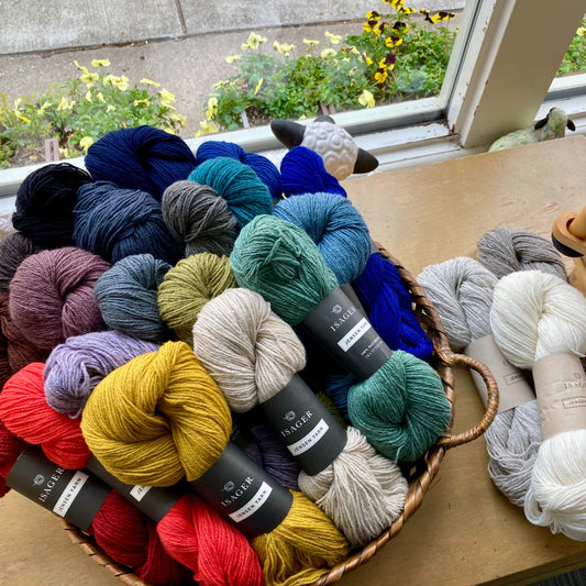 Colorful skeins of Isager Jensen yarn in a basket on a wooden table, before a window.
