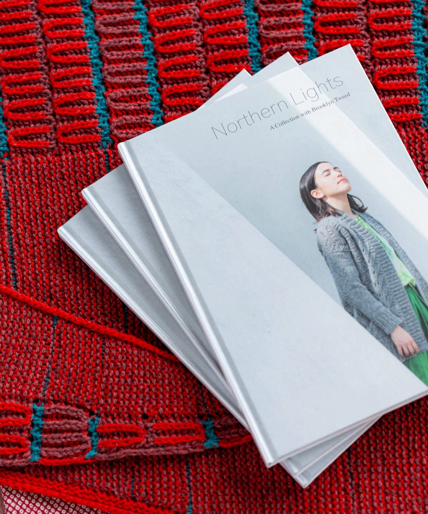Copies of Brooklyn Tweed’s Northern Lights book lying on a red and teal handknit shawl.