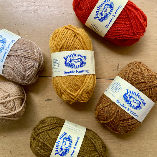 Collection of Jamieson's Double Knitting yarn balls in various colors on a wooden surface.