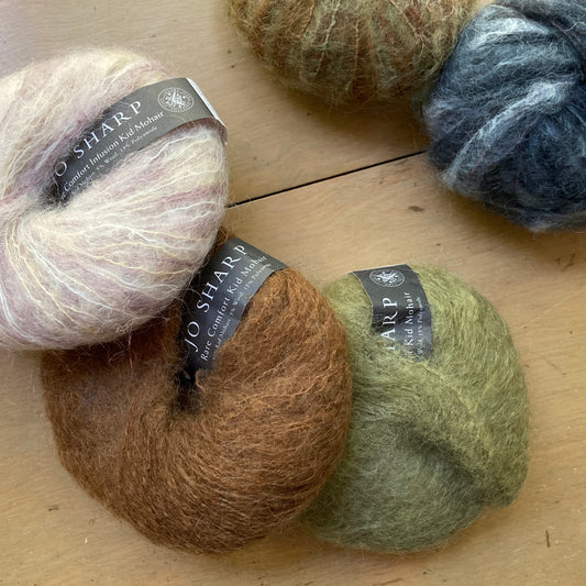 Balls of fuzzy Jo Sharp mohair yarn in muted earth tones.
