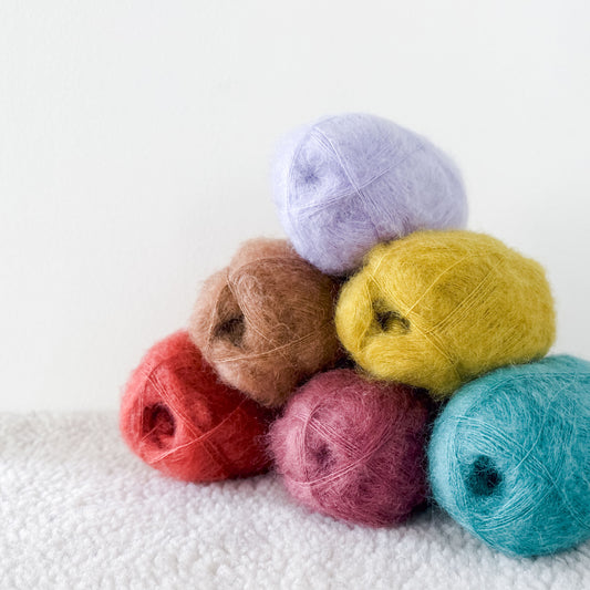 A pyramid of Kelbourne Woolens' Harmony silk mohair yarn stacked in vibrant colors against a white backdrop.