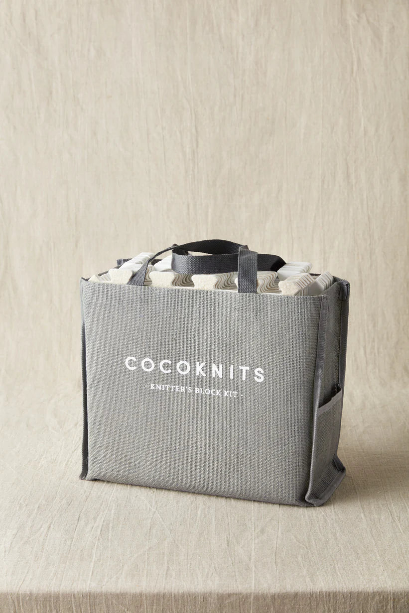 Gray jute tote filled with blocking tools on a beige surface.