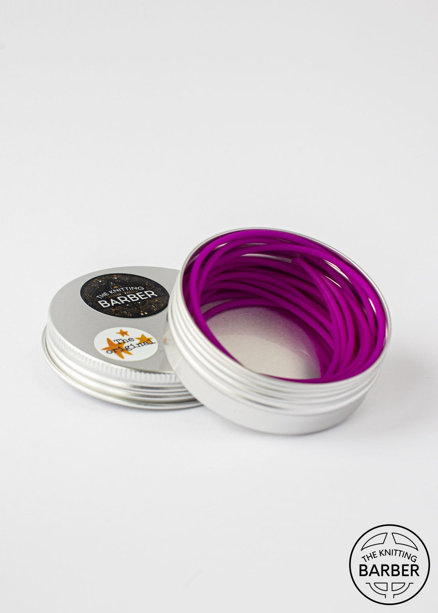 Round silver tin lying open beside its lid, showing mauve Knitting Barber Cords coiled inside.