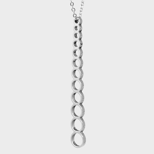 A long stainless steel pendant (attached to a neck chain) with vertical connecting holes to measure knitting needle sizes.