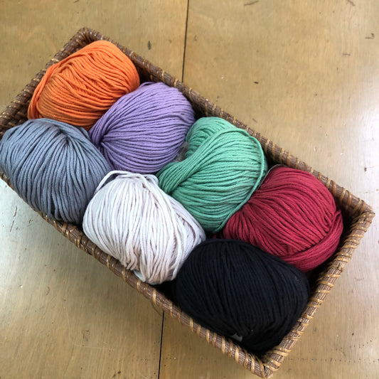 Balls of Lana Grossa Organico cotton yarn in red, black, orange, purple, gray, cream, and green.