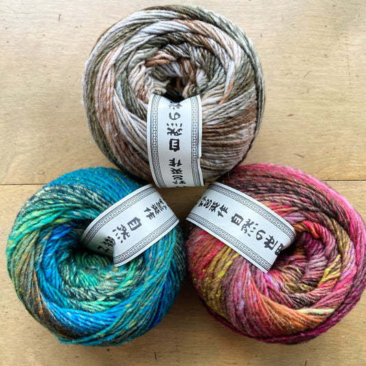 Three colorful balls of self striping Noro Ito yarn arranged on a wooden surface.
