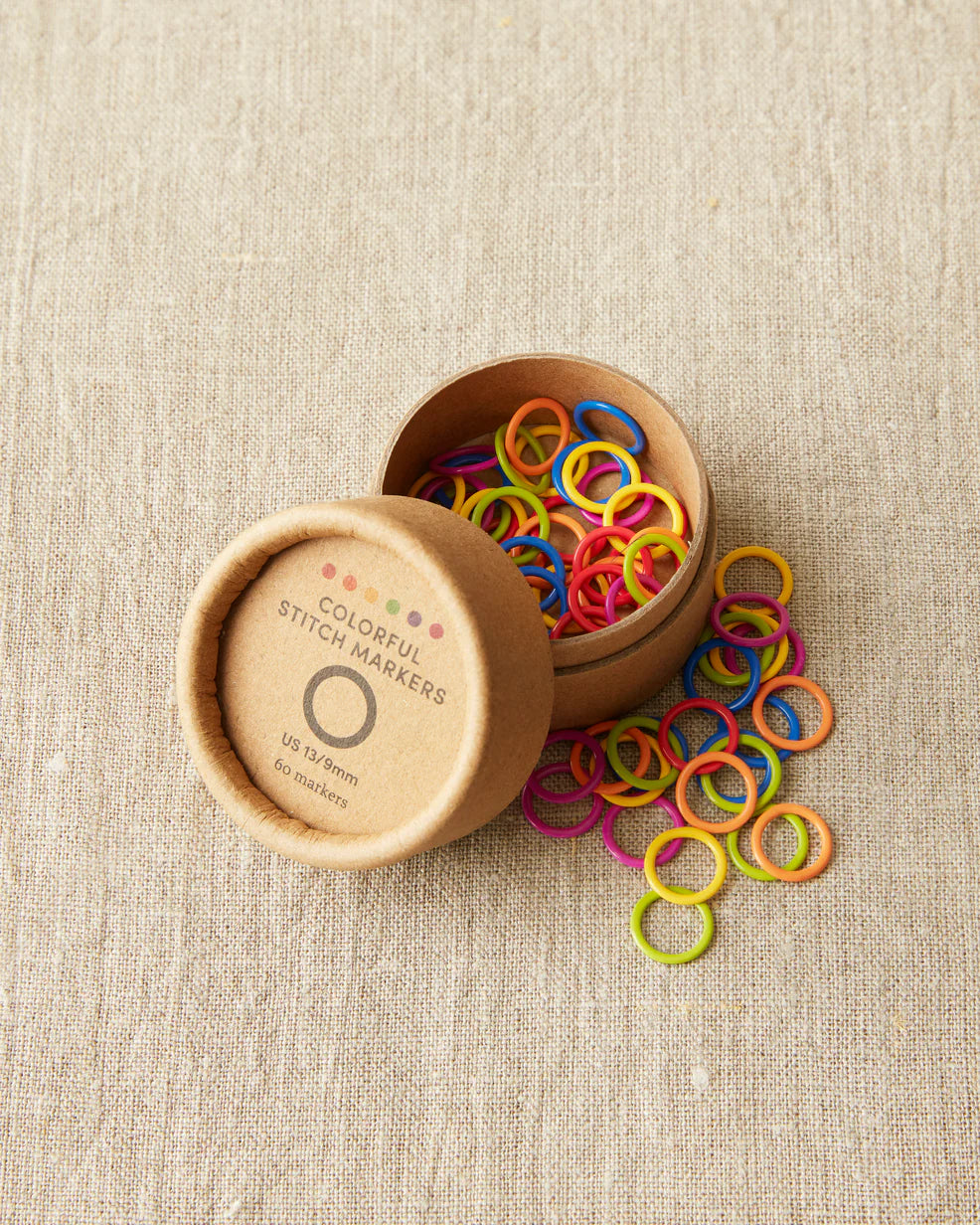 Open box of colorful cocoknits stitch markers on a light gray surface.