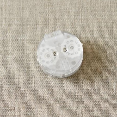Translucent white plastic row counter on a beige background.