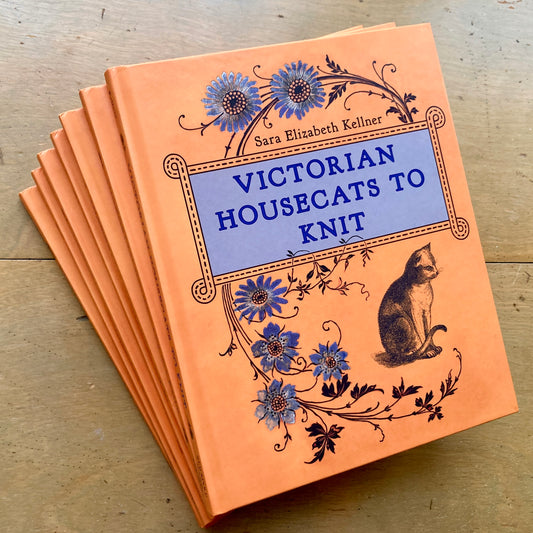 A stack of orange hardcover books on a wooden surface - Victorian Housecats to Knit, by Sara Elizabeth Kellner