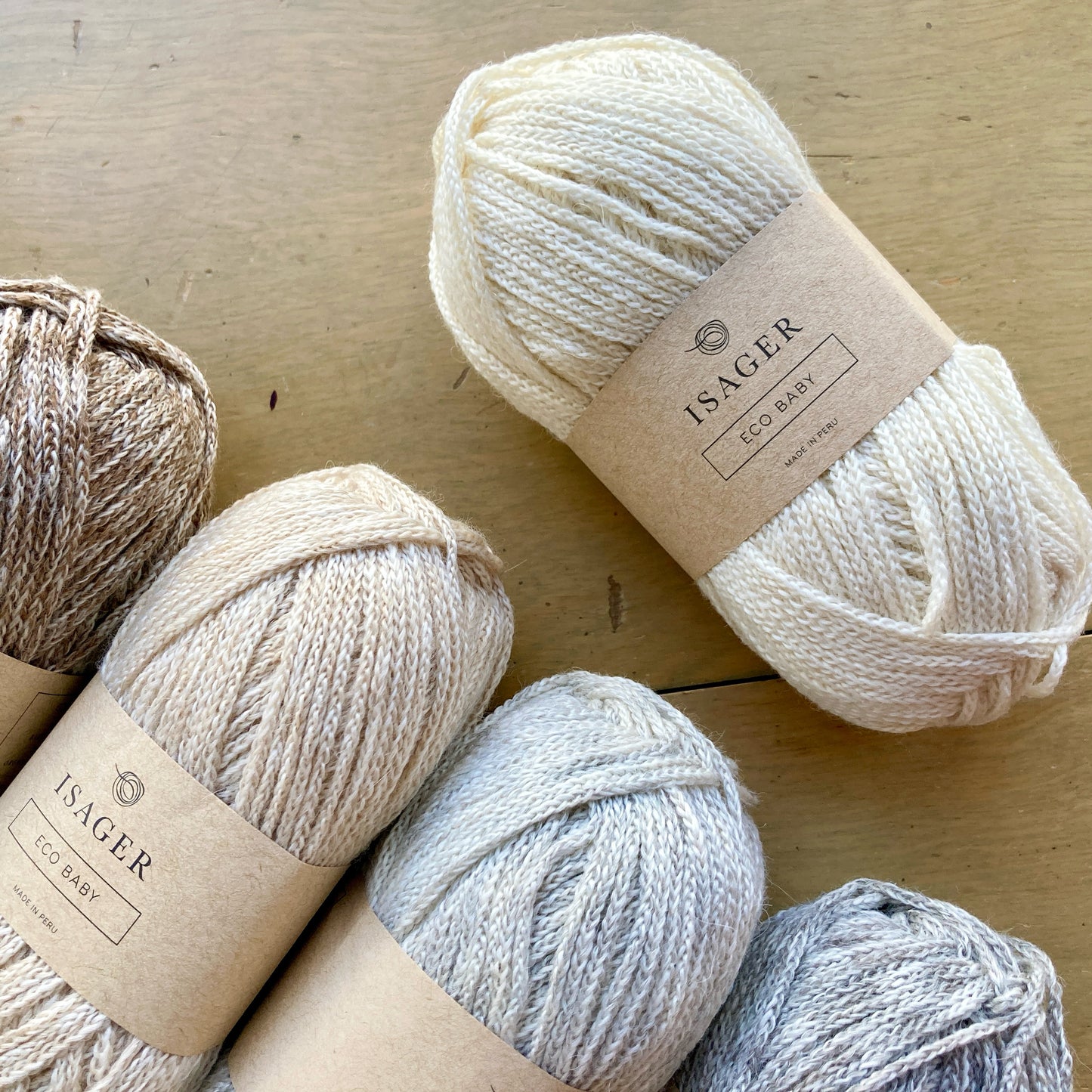 Natural colored balls of Isager Eco Baby yarn arranged on a wooden surface.