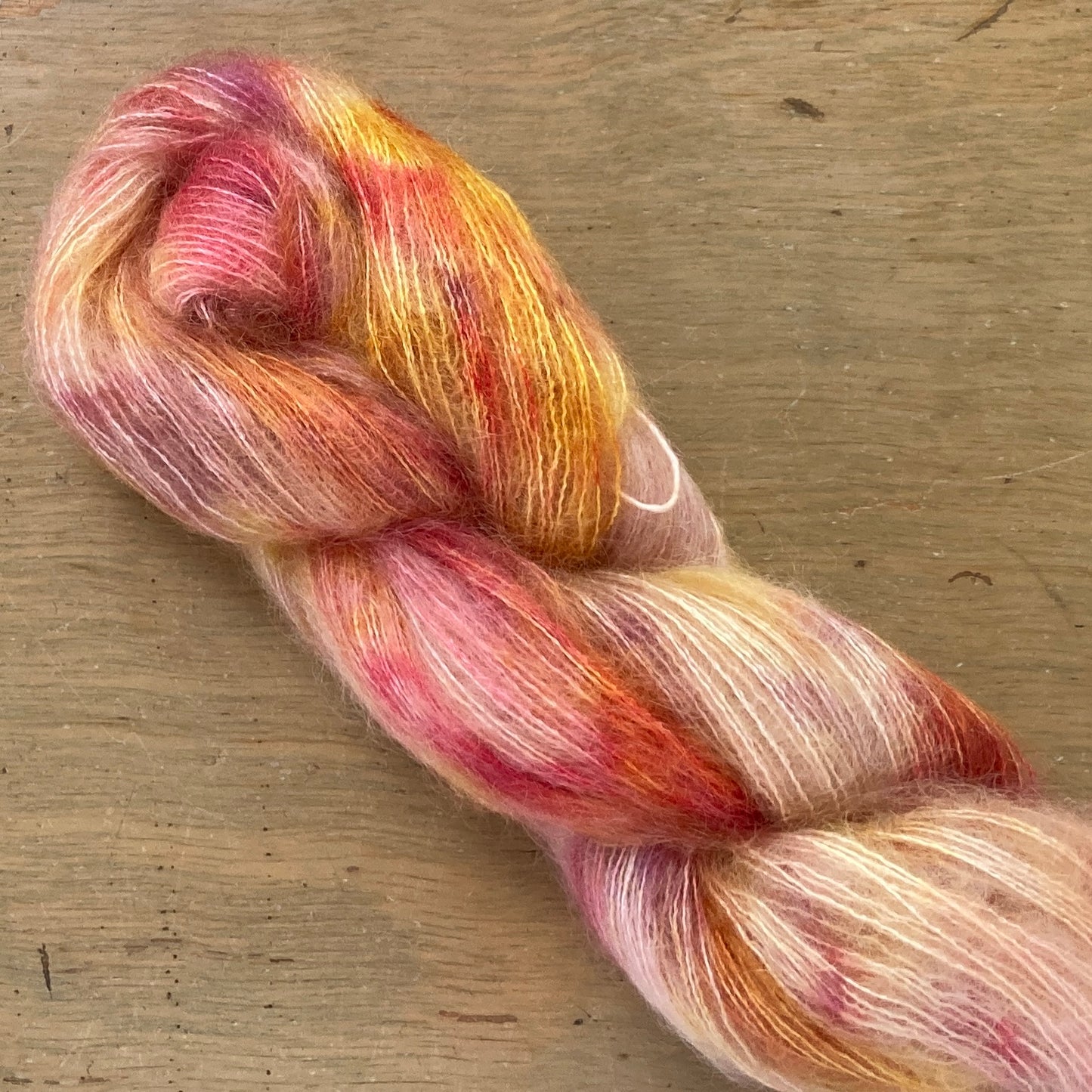 Speckled red, peach, and gold skein of Fleece Artist / Hand Maiden Superkid Silk yarn, colorway Honeycomb
