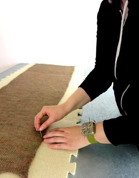 Close up on a pair of hands pinning knit fabric to blocking tiles.