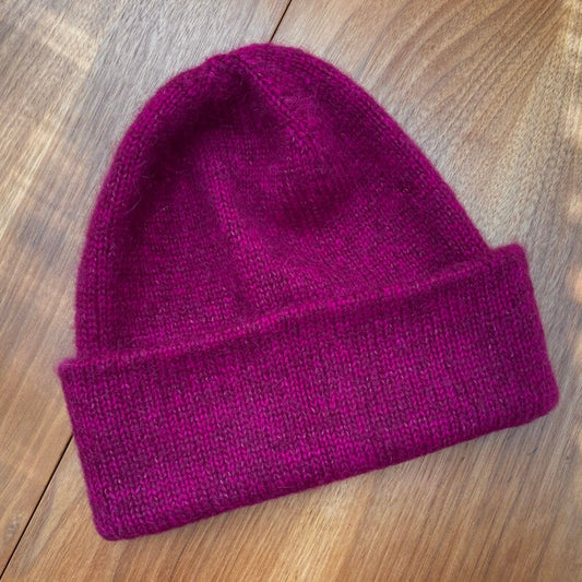 Raspberry pink PetiteKnit "Oslo Hat" on a wooden surface, knit with Kelbourne Woolens Perennial and Fyberspates Cumulus yarn.