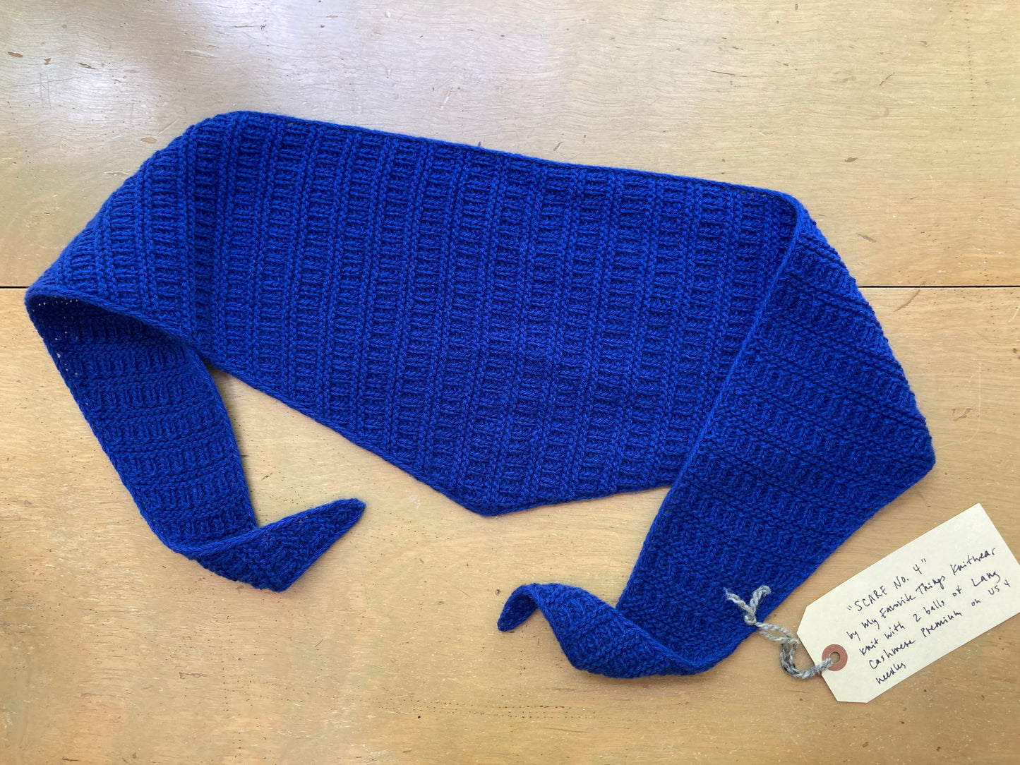 Cobalt blue textured triangular scarf lying on a wooden surface. 