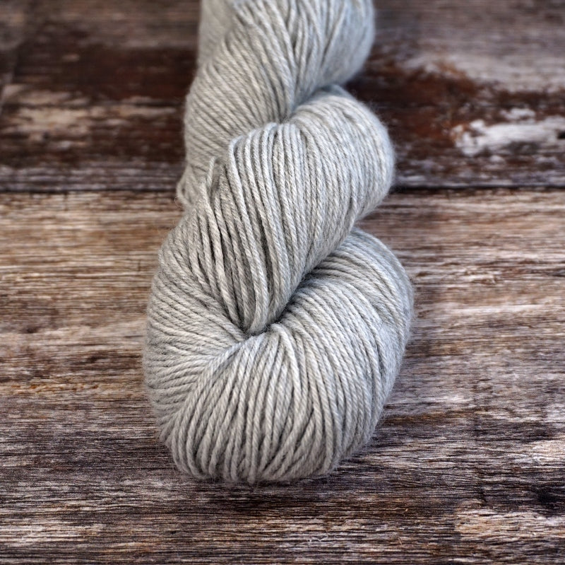 Light gray skein of CoopKnits Socks Yeah! yarn on a wooden surface. 