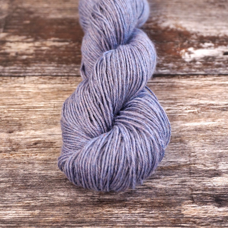 Lavender skein of CoopKnits Socks Yeah! yarn on a wooden surface. 