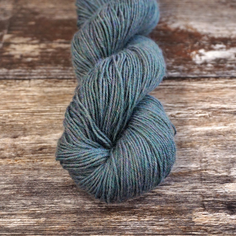 Heathered gray skein of CoopKnits Socks Yeah! yarn on a wooden surface. 