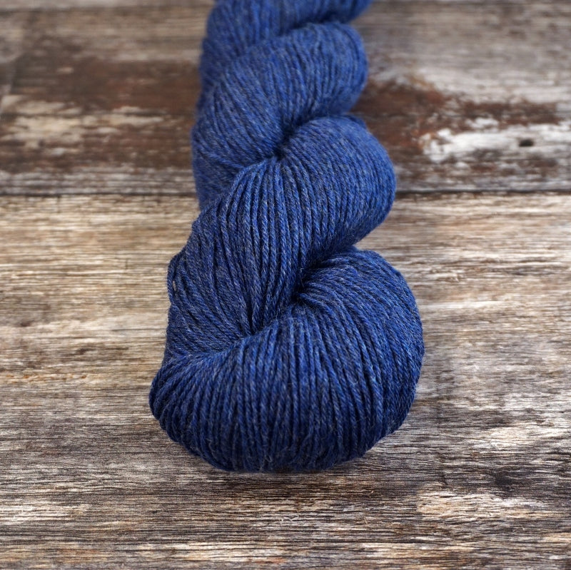 Dark blue skein of CoopKnits Socks Yeah! yarn on a wooden surface. 