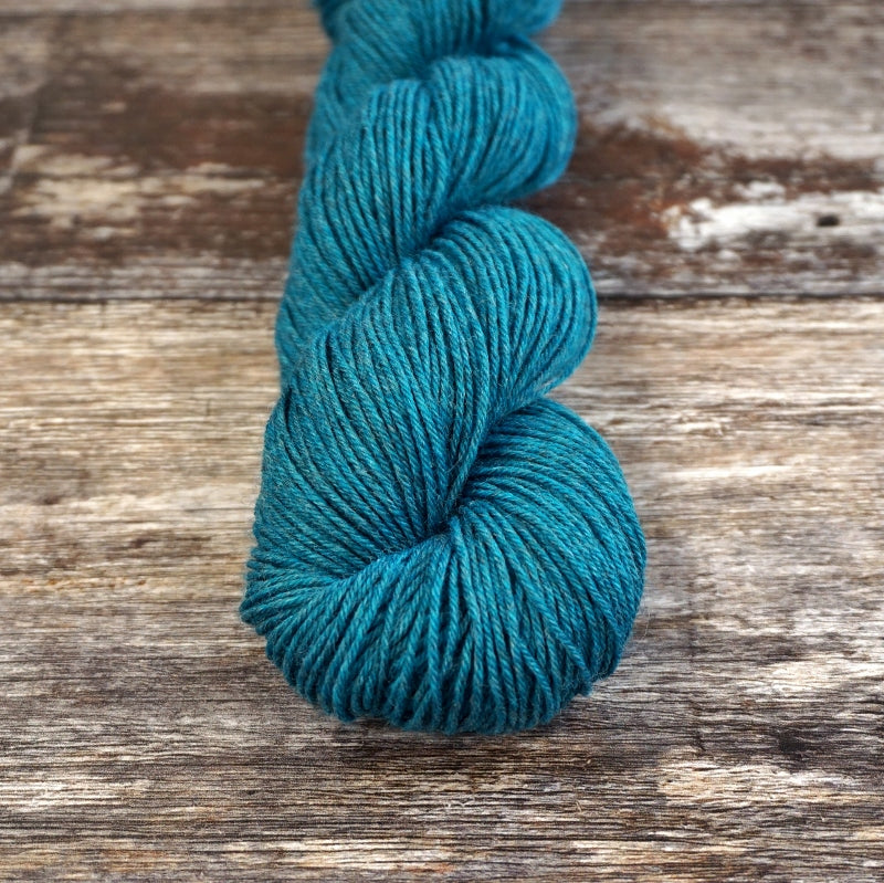 Teal skein of CoopKnits Socks Yeah! yarn on a wooden surface. 