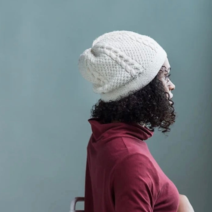 A young Black woman in profile, wearing a gray cabled hat. 