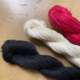 Black, ivory, and red skeins of M&K Linen yarn. 