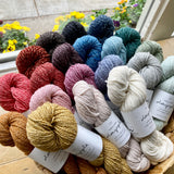 Colorful skeins of Brooklyn Tweed Dapple yarn in a basket on a table before a window. 