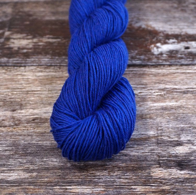 Cobalt blue skein of CoopKnits Socks Yeah! yarn on a wooden surface. 