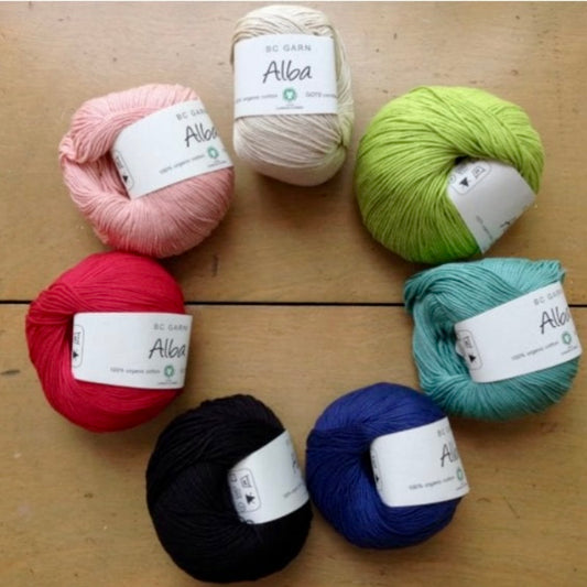 Collection of colorful balls of BC Garn Alba yarn arranged in a circle on a wooden surface. 