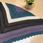 Triangular crocheted shawl lying flat on a table near a potted plant. 