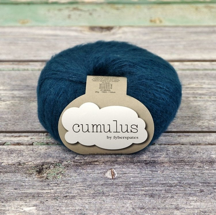 Ball of dark blue green Fyberspates Cumulus yarn on a wooden surface. 