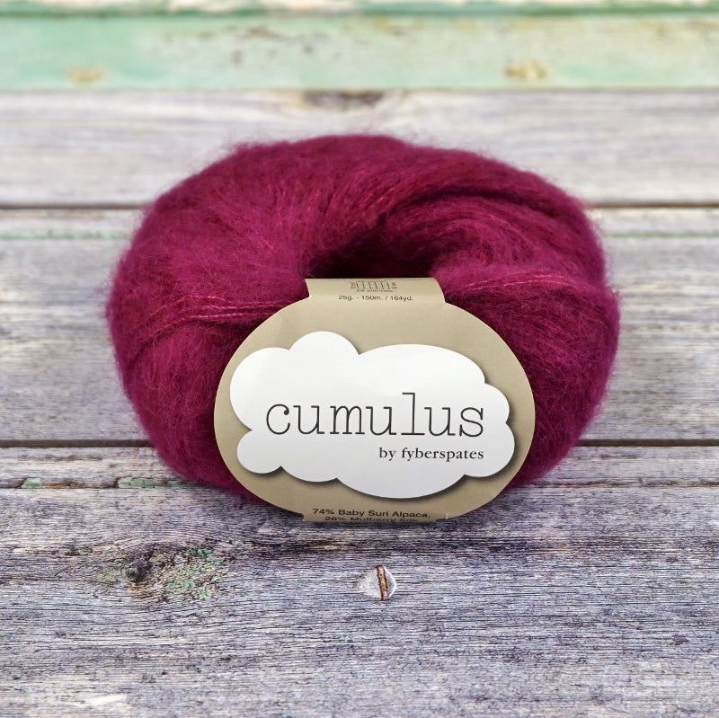 Ball of dark magenta Fyberspates Cumulus yarn on a wooden surface. 