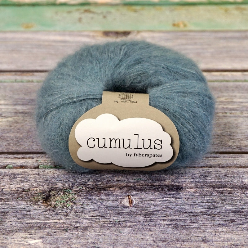 Ball of denim blue Fyberspates Cumulus yarn on a wooden surface. 