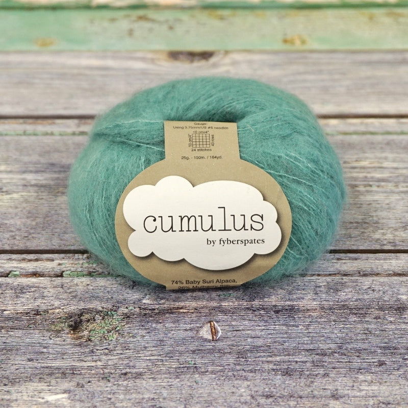 Ball of sea green Fyberspates Cumulus yarn on a wooden surface. 