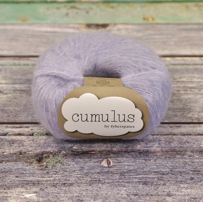 Ball of pale purple gray Fyberspates Cumulus yarn on a wooden surface. 