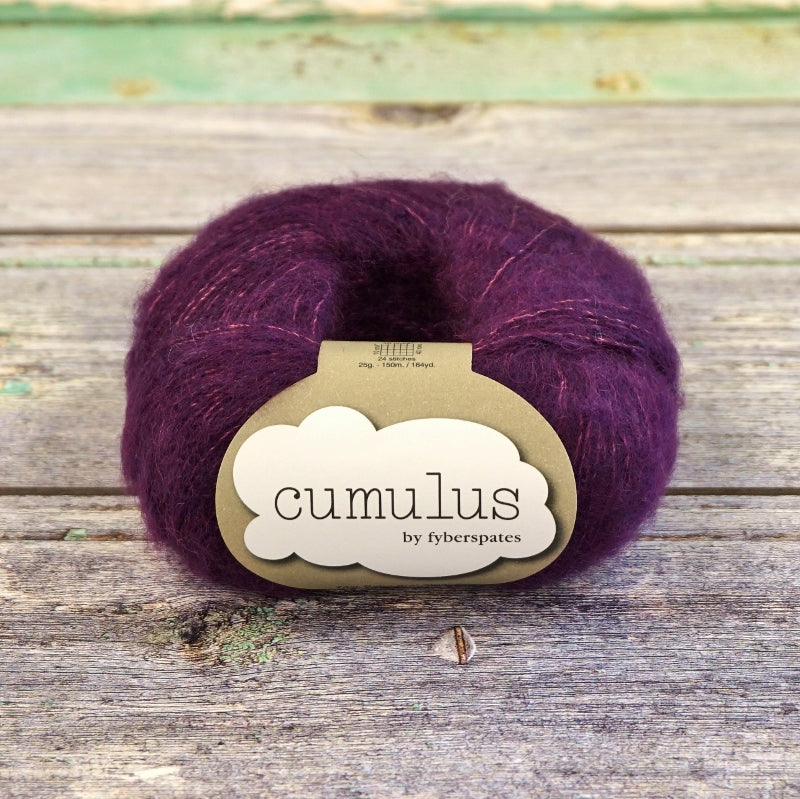 Ball of deep purple Fyberspates Cumulus yarn on a wooden surface. 