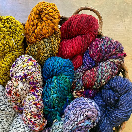 Colorful skeins of marled hand dyed Malabrigo Caracol yarn in a basket on a wooden surface. 