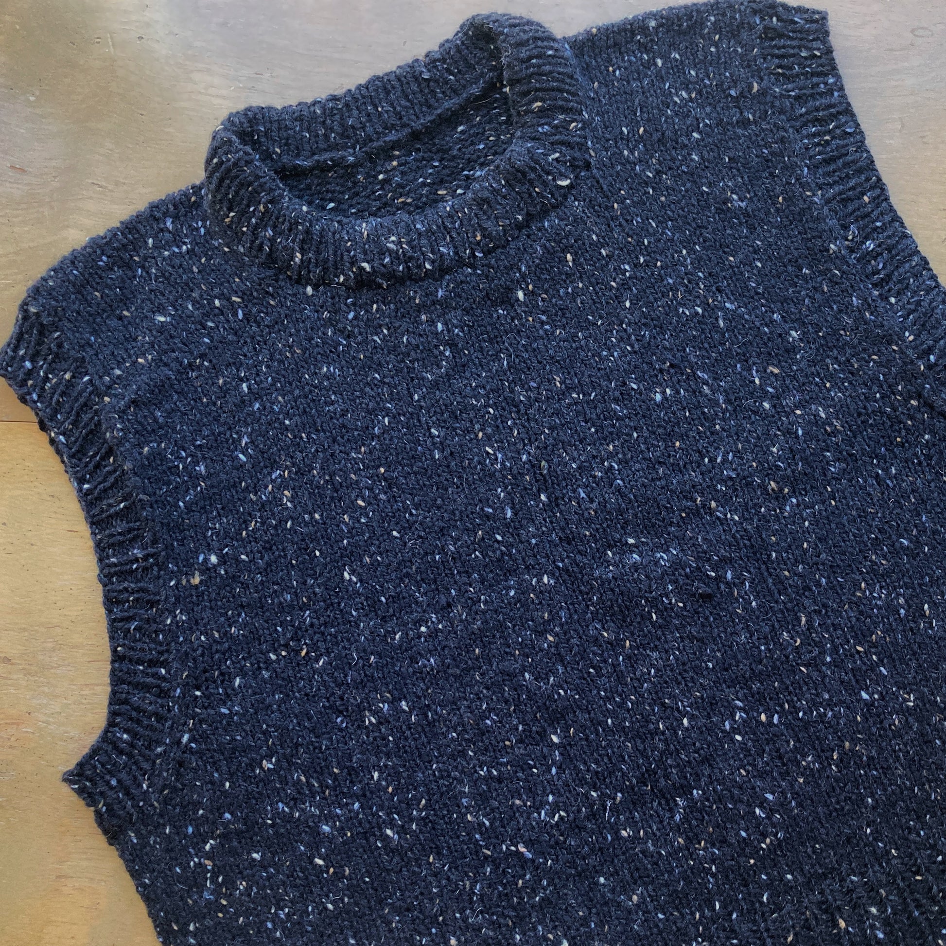 Close up on a black tweed handknit vest on a wooden surface. 