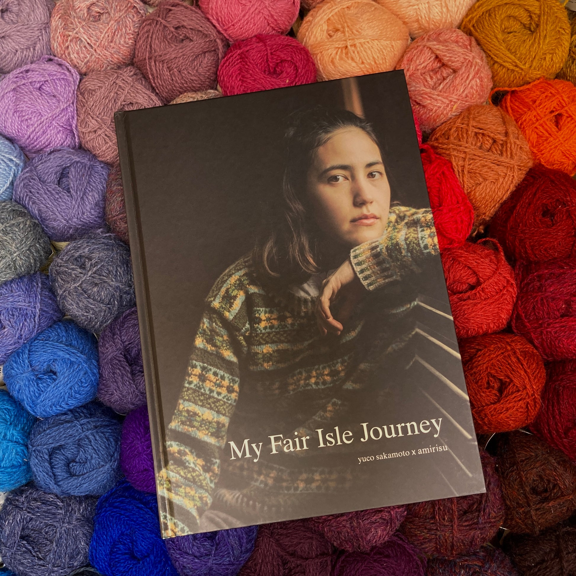 Yuco Sakamoto’s My Fair Isle Journey book lying on a rainbow of colorful Shetland wool yarn. 