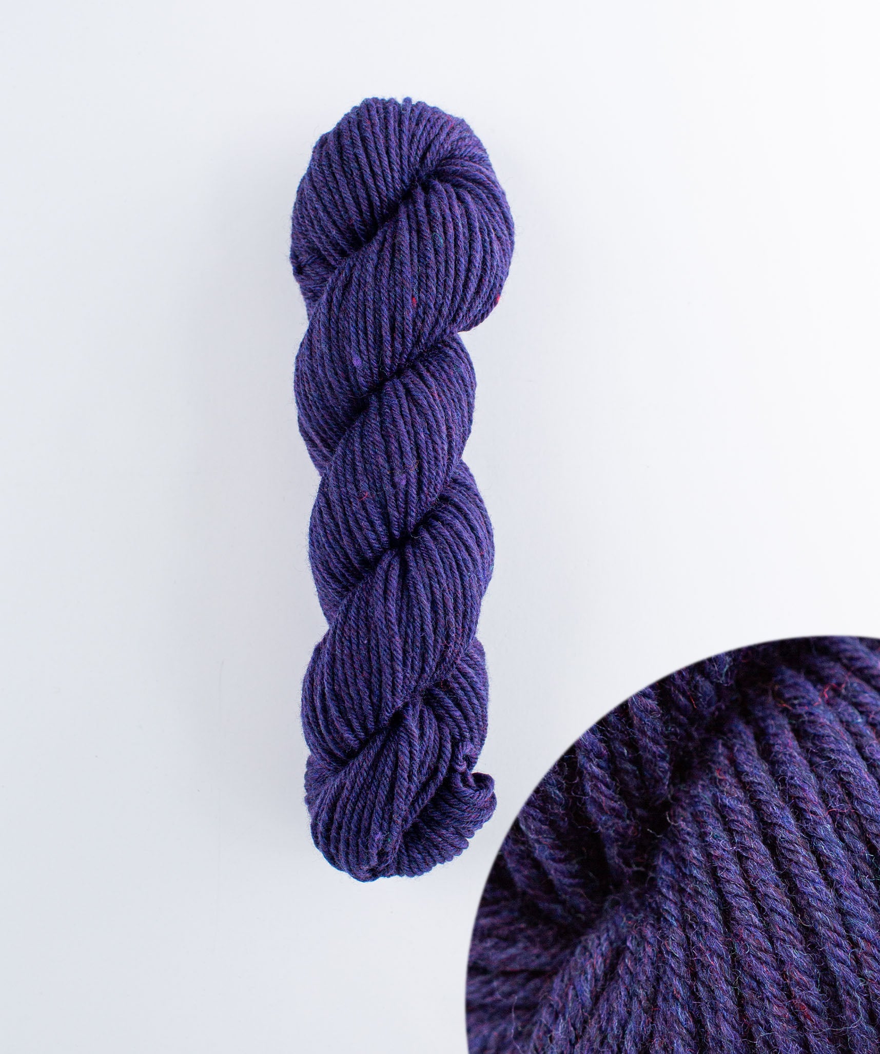 A skein of violet purple slightly tweedy yarn with specs of red and blue.