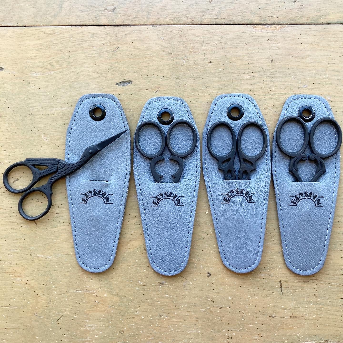 Four sets of black matte Bryspun scissors in gray leather sheaths. 