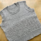 Fuzzy textured handknit gray vest, lying on a wooden surface. 