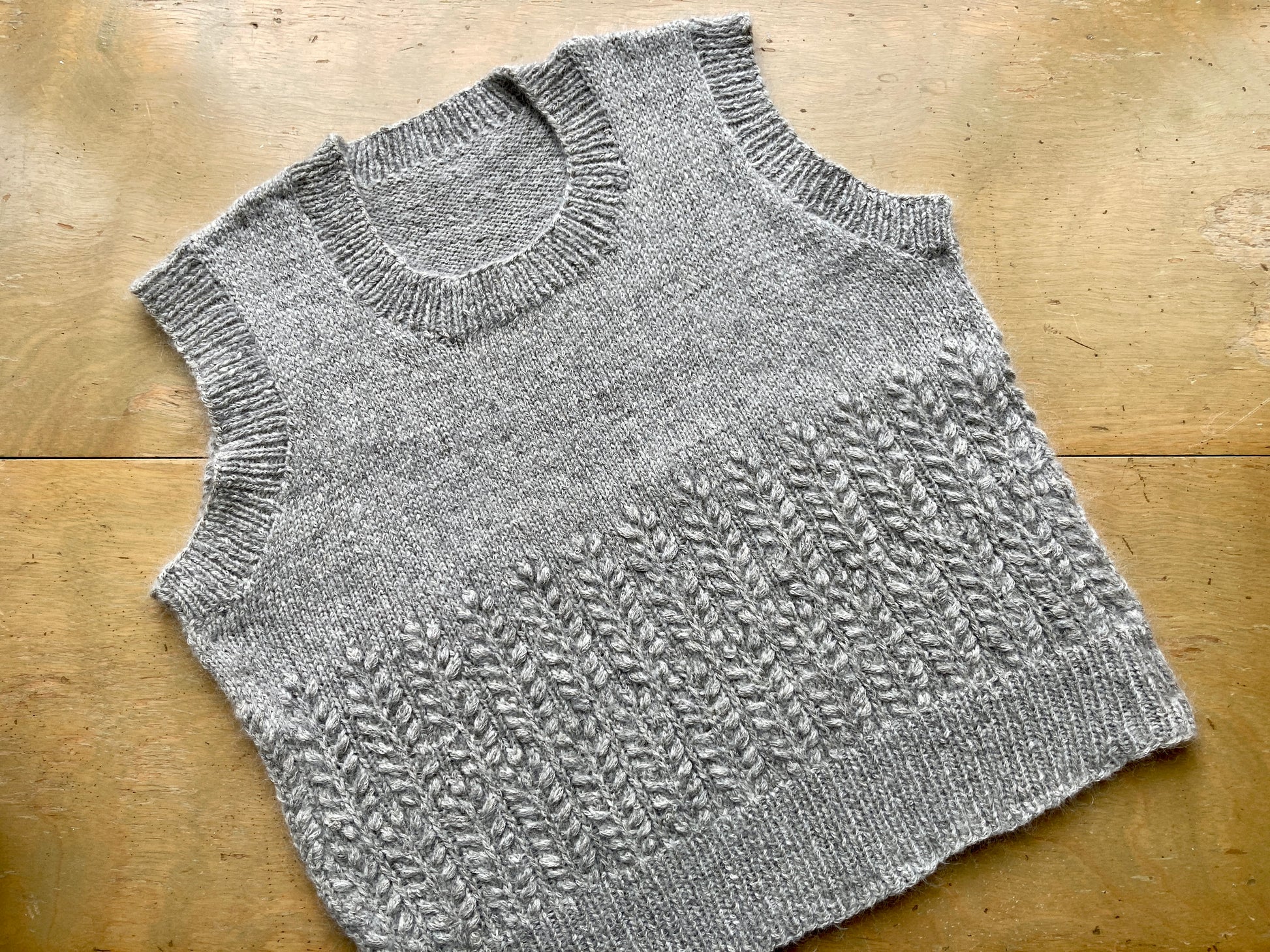 Fuzzy textured handknit gray vest, lying on a wooden surface. 