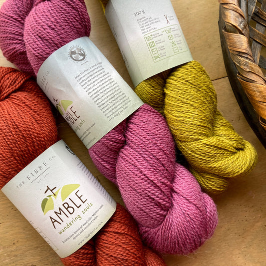 Close up on three colorful skeins of Fibre Co. Amble yarn on a wooden surface. 