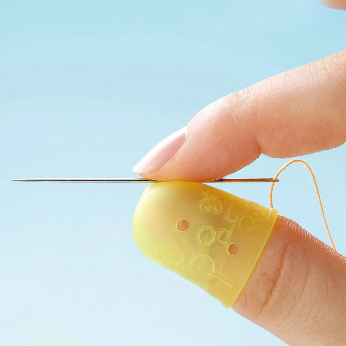 Close-up image of thumb and pointer finger holding a sewing needle, with the Clover Flexible Thimble worn on the thumb. 