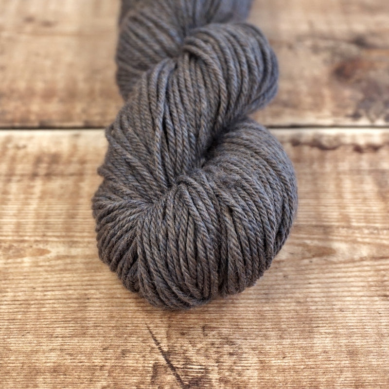 Slate gray skein of CoopKnits Socks Yeah! DK yarn on a wooden surface. 