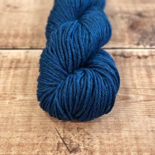 Dark teal blue skein of CoopKnits Socks Yeah! DK yarn on a wooden surface. 