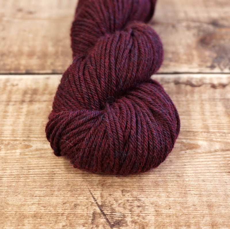 Maroon skein of CoopKnits Socks Yeah! DK yarn on a wooden surface. 