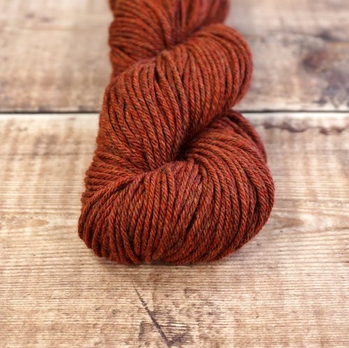 Rust red skein of CoopKnits Socks Yeah! DK yarn on a wooden surface. 