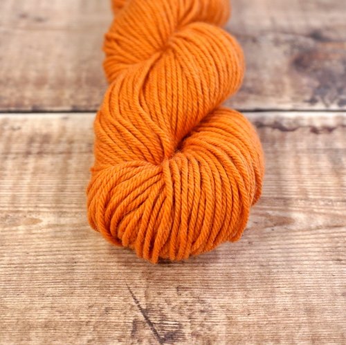 Pumpkin orange skein of CoopKnits Socks Yeah! DK yarn on a wooden surface. 