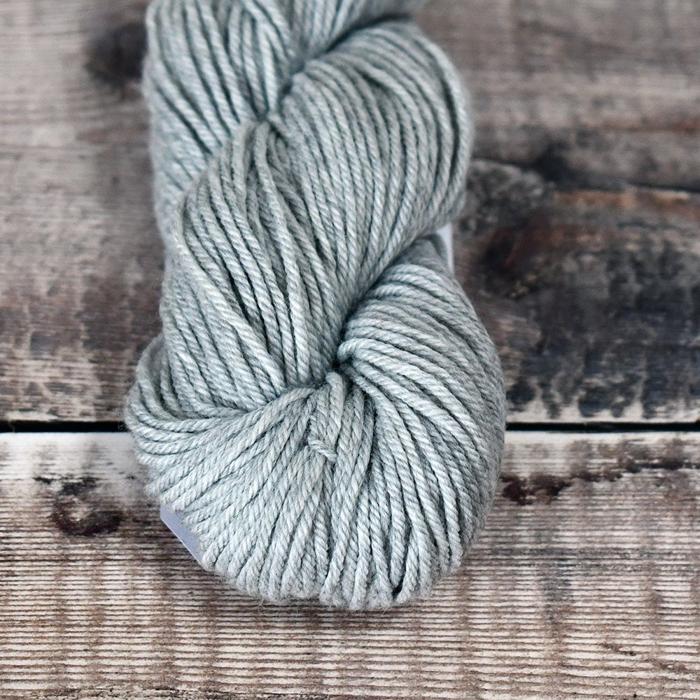 Silver skein of CoopKnits Socks Yeah! DK yarn on a wooden surface. 